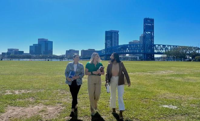 Three female law students walking across a green park, with a blue bridge in the background.